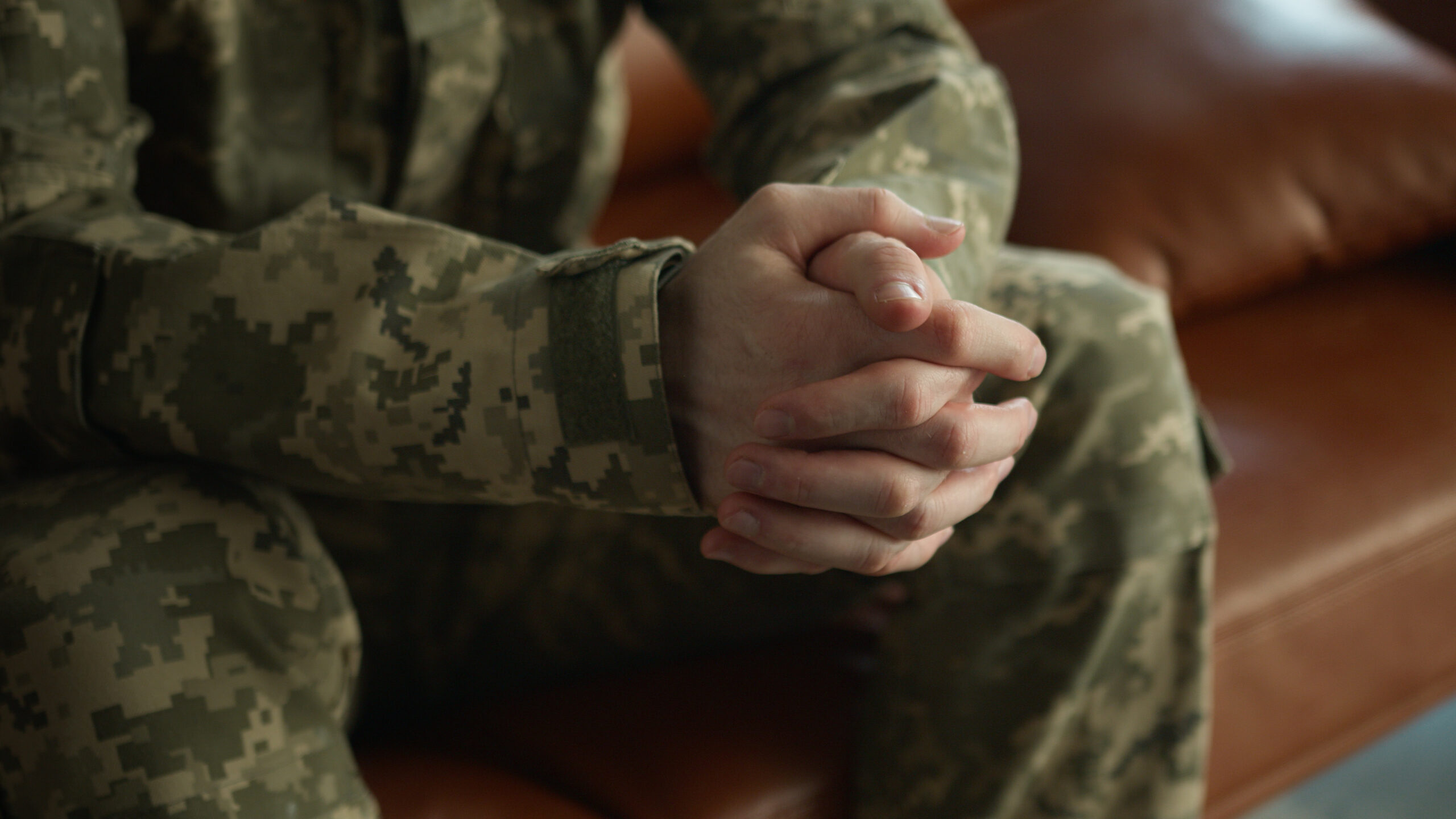 Unbekannter, nervöser, kaukasischer Offizier, Soldat, Patriot, Veteran in ukrainischer Tarnuniform, die Hände gefaltet, die Handflächen geballt, sitzt auf einer Couch in einer Klinik. Nachkriegsstresstherapie