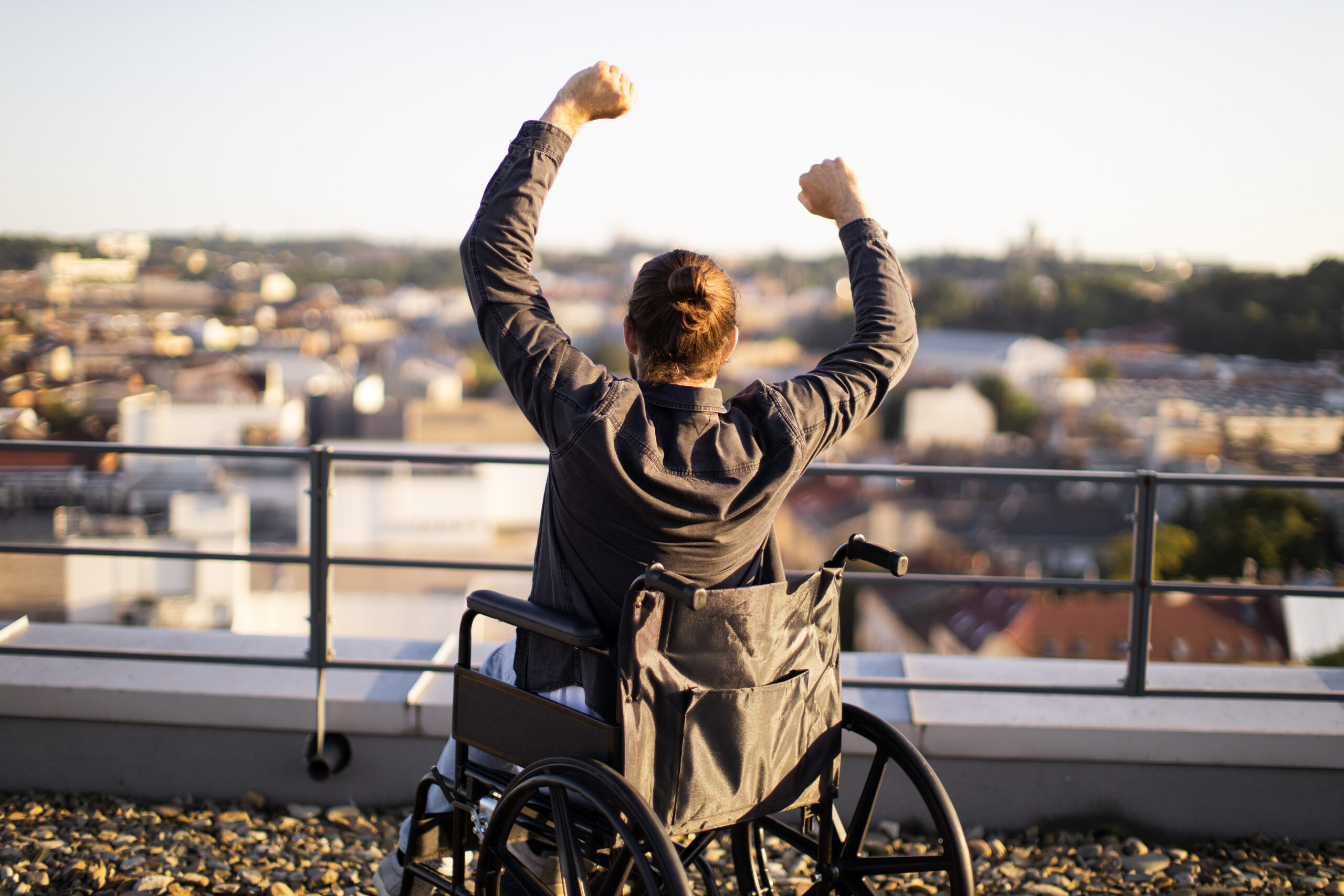 Man in wheelchair raising arms in triumph overlooking city