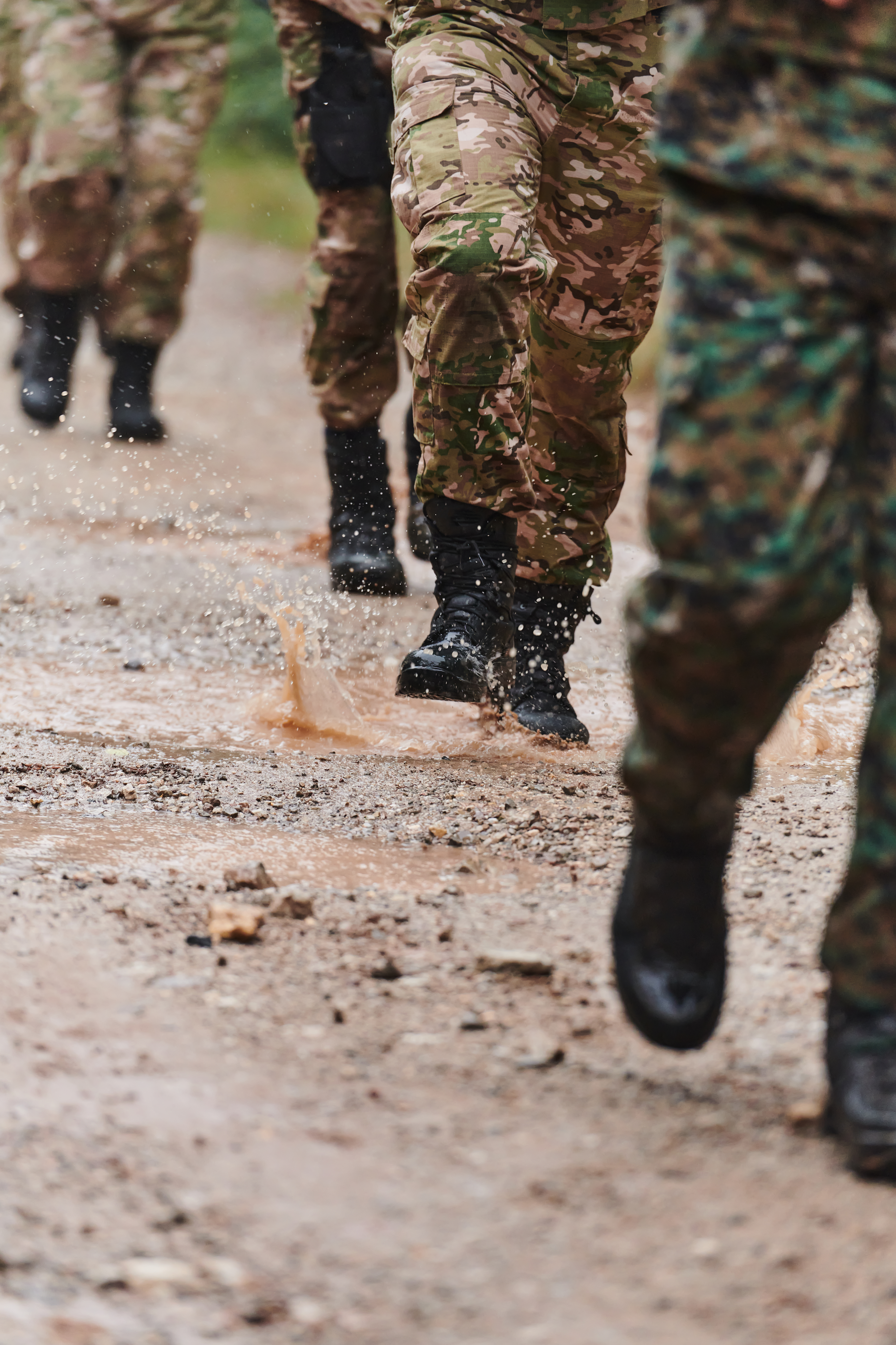 Close up photo, the resilient legs of elite soldiers, clad in camouflage boots, stride purposefully along a hazardous forest path as they embark on a high-stakes military mission