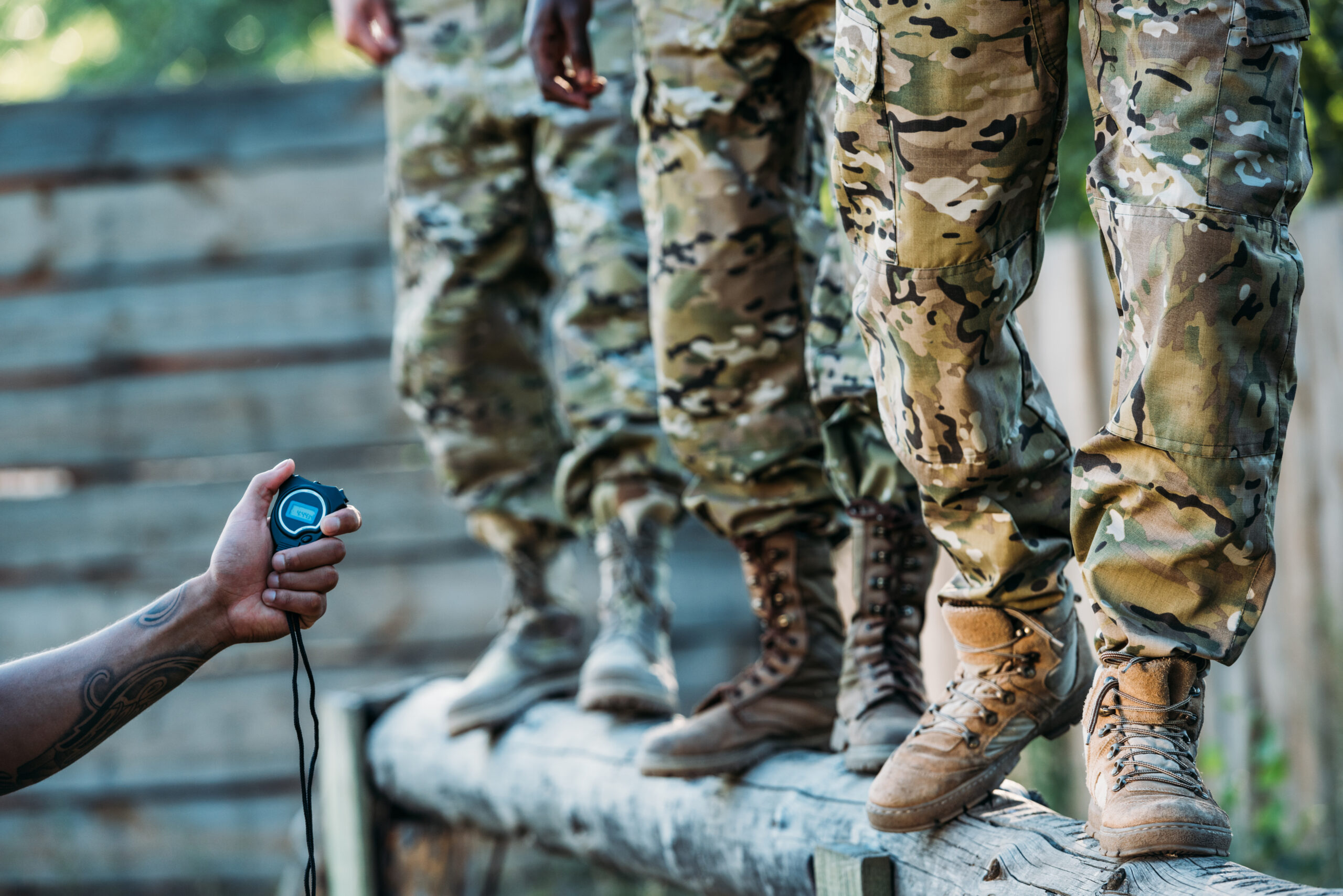partial view of tactical instructor with stop watch examining multiracial soldiers during obstacle